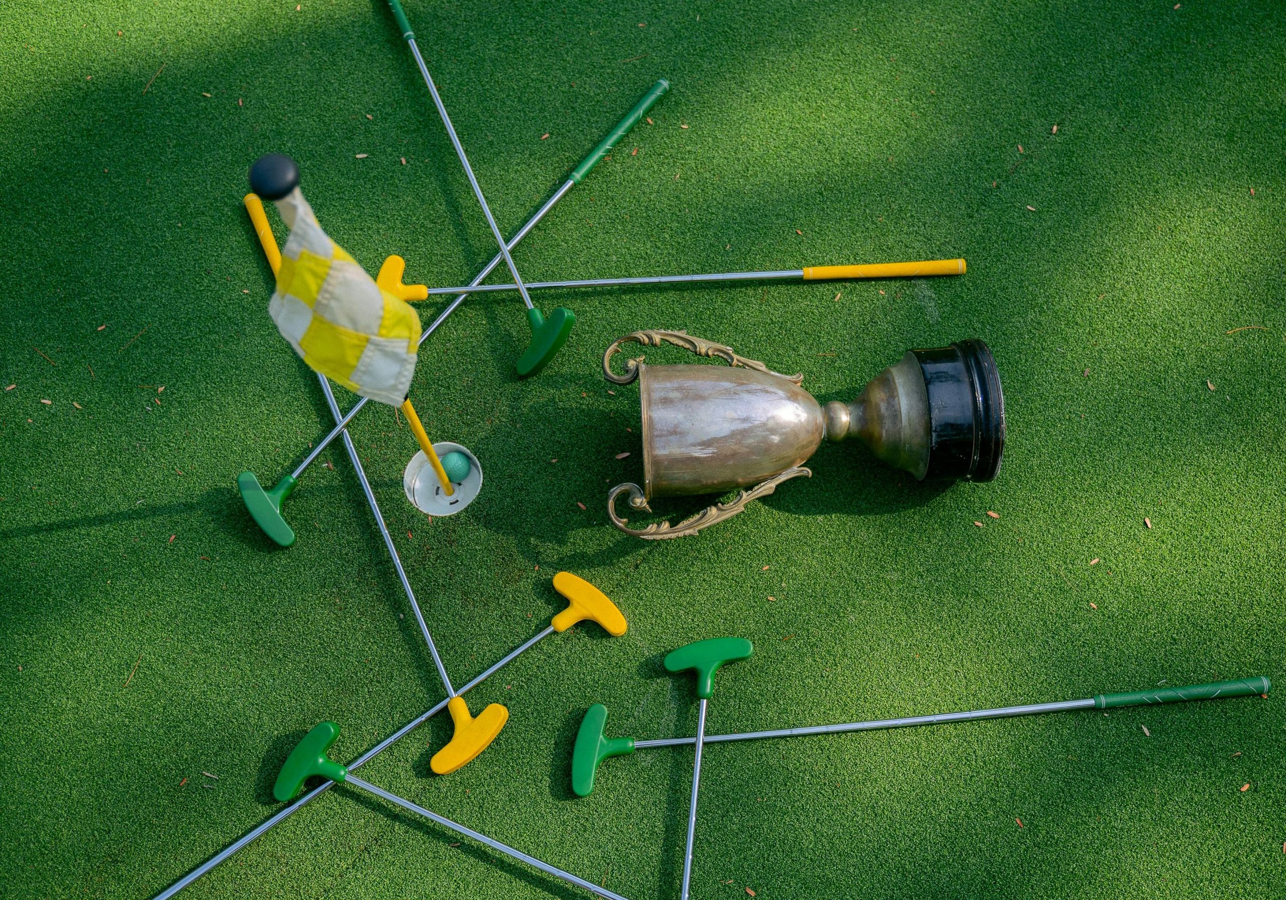 Mini golf setup with colorful putters, a cup, and a flag on green turf. Ideal for casual sports and recreation themes.